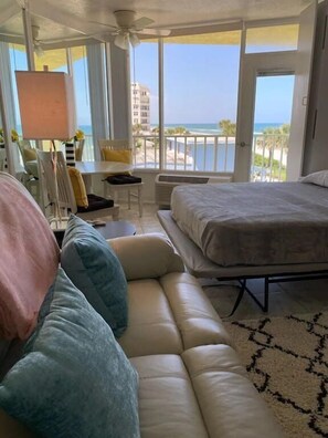 Een kamer met een bed, een bank, een tafel en een stoel. Grote ramen bieden uitzicht op het strand en de oceaan.