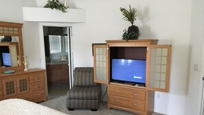 A bedroom with a bed, a TV on a wooden cabinet, a chair, and a dresser. - 1868 Poppy Cir (The Villages)