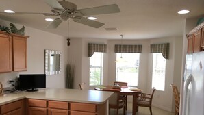 A kitchen with a central island, wooden cabinets, a ceiling fan, and a dining area with a table and chairs. - 1868 Poppy Cir (The Villages)