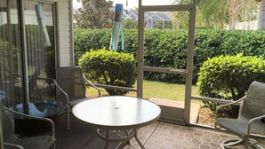A covered patio with a glass table and chairs, a ceiling fan, and a view of a well-maintained garden and house. - 1868 Poppy Cir (The Villages)