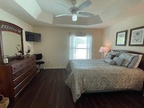 A bedroom with a bed, dresser, vanity, ceiling fan, window with blinds, and framed pictures on the wall. - 9238 SE 166th Sprung Ln (The Villages)