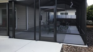 Un patio cubierto con cerramiento de vidrio, mobiliario exterior y vista al jardín trasero.