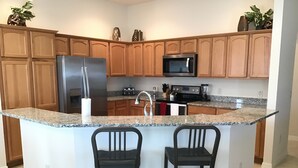 Una cocina con armarios de madera, un refrigerador de acero inoxidable, un microondas, una estufa y dos taburetes de bar.