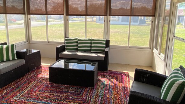 Une véranda avec un ventilateur de plafond, de grandes fenêtres, un canapé, une table basse et un tapis coloré.