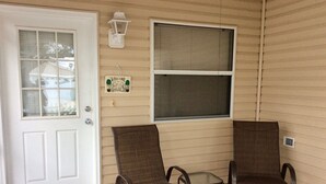 A porch with two wicker chairs and a small table, a white door, and a window with blinds. - 2468 Southern Oak St (The Villages)