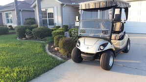 Une voiturette de golf est garée devant une maison dont la pelouse est bien entretenue, avec une boîte aux lettres et une porte de garage.