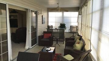 A covered patio area with wicker furniture, a table, and a ceiling fan.