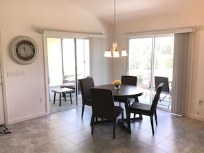Een eetruimte met een ronde tafel, zes stoelen, een kroonluchter en een wandklok.
