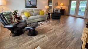 A living room with a beige sofa, a black leather chair, a small table with a lamp, and a framed picture on the wall. - 427 Santa Clara Cir (Lady Lake)