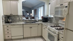 A kitchen with white cabinets, a granite countertop, a stove, a microwave, and a sink. - 2066 Duval Ct (The Villages)