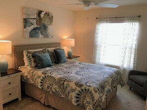 A bedroom with a bed, two bedside tables, a ceiling fan, a window with sheer curtains, and a partial view of a gray armchair. - 2315 Jans Ter (Wildwood)
