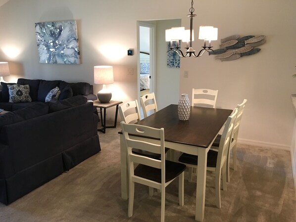 A dining area with a dark wooden table and white chairs, a black sofa with patterned cushions, a lamp, and a wall-mounted fish decoration. - 2315 Jans Ter (Wildwood)