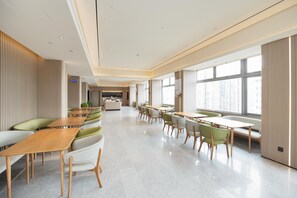 Um saguão de hotel moderno com um balcão de recepção alongado, áreas de estar com cadeiras verdes e brancas, e grandes janelas com vista para a cidade.