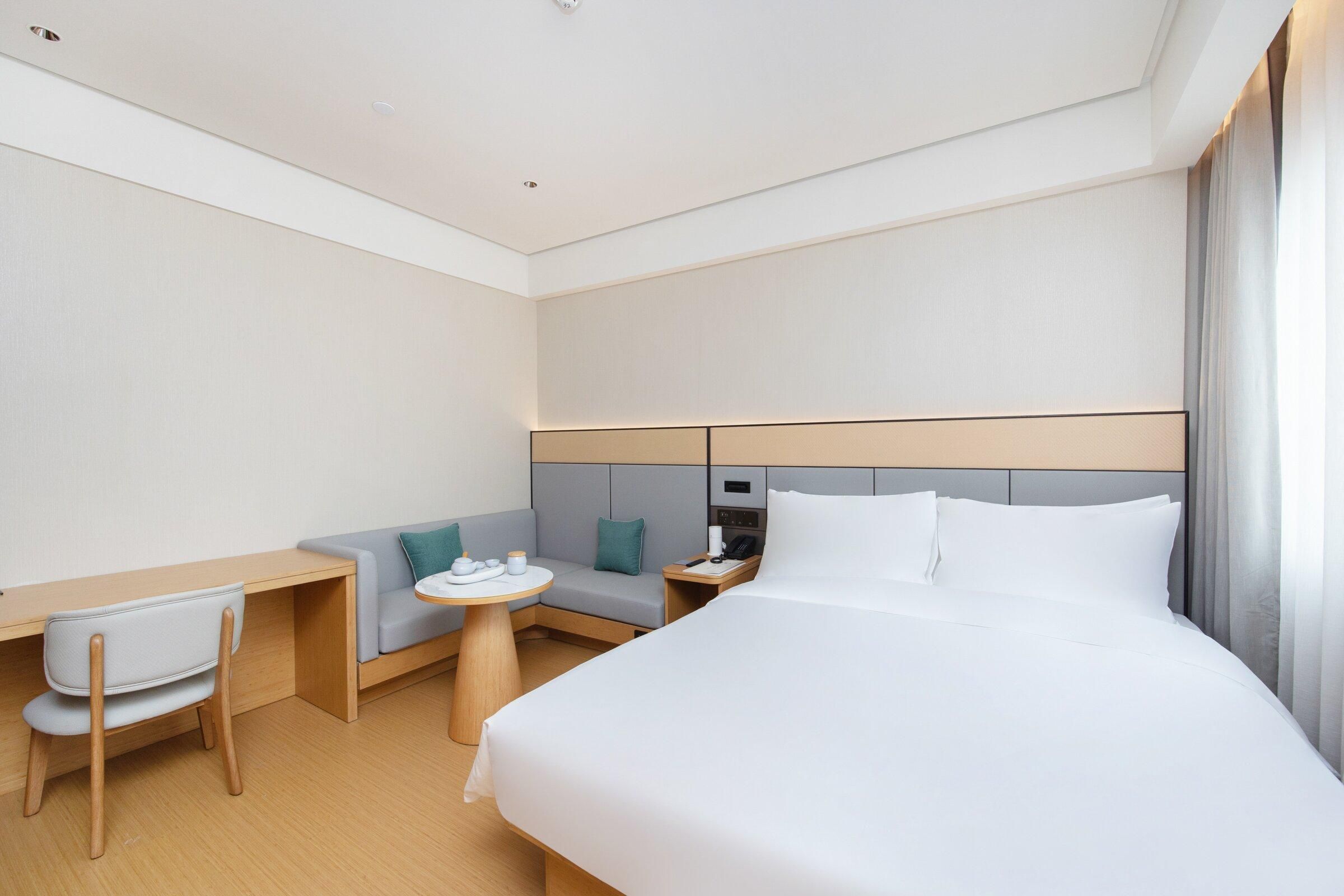 Una habitación de hotel moderna con cama, escritorio, silla, mesita y sofá.