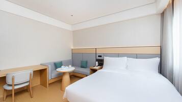 Una habitación de hotel moderna con cama, escritorio, silla, mesita y sofá.
