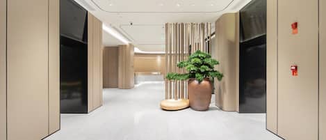 A modern hallway with a large potted plant, a round table, and a wall-mounted fire alarm.
