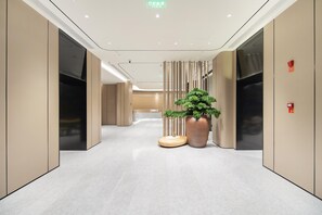 A modern hallway with a large potted plant, a round table, and a wall-mounted fire alarm. - Ji Hotel Shenzhen Huaqiang North Electronic Buildi (Shenzhen)