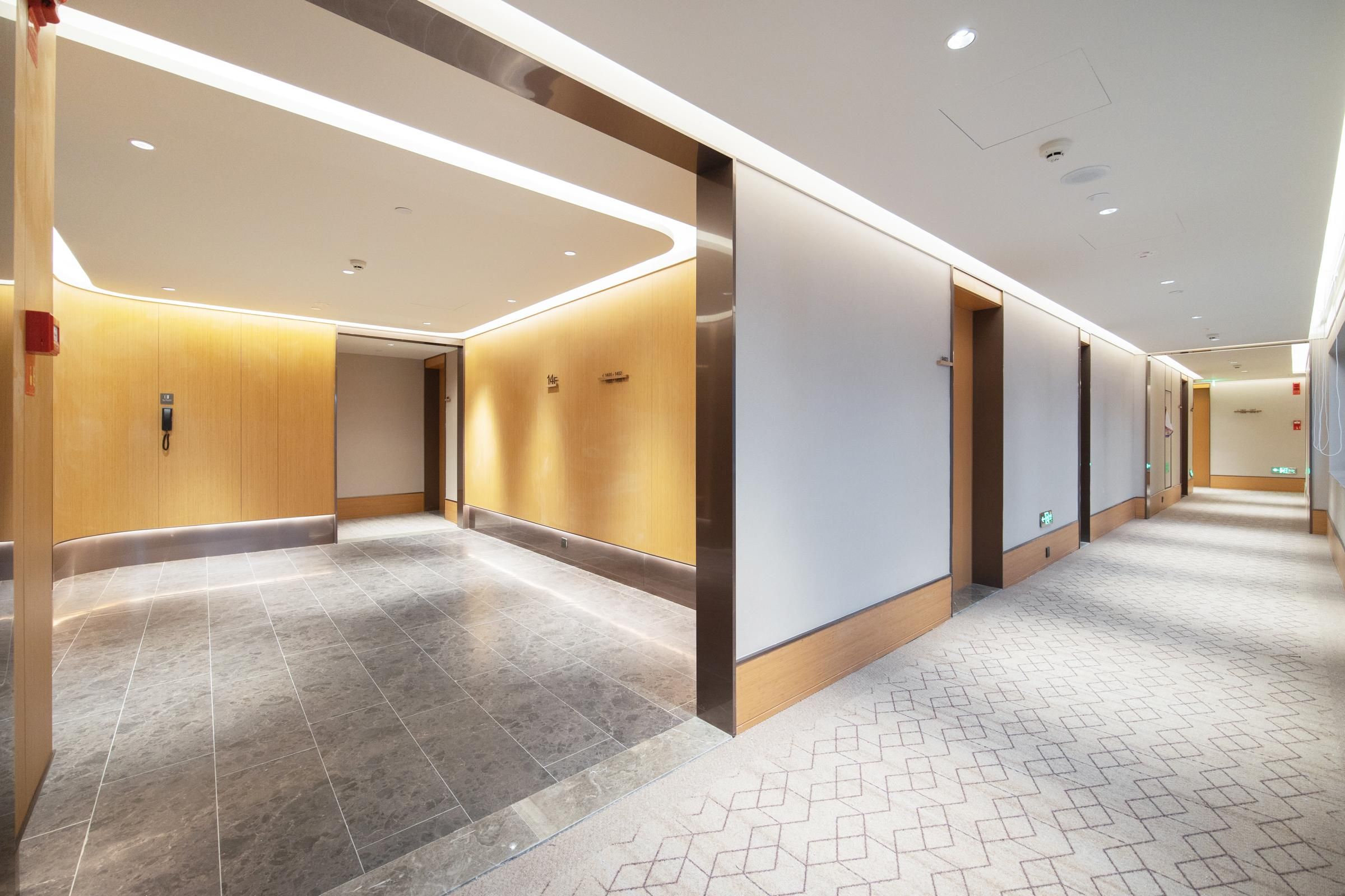 Un pasillo moderno de hotel con suelo de baldosas, paneles de madera e iluminación empotrada.