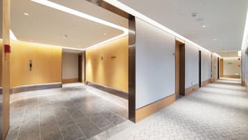 Un pasillo moderno de hotel con suelo de baldosas, paneles de madera e iluminación empotrada.