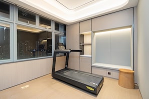 A modern room with a treadmill, a window with a city view, built-in shelving, and a small wooden stool. - Ji Hotel Shenzhen Huaqiang North Electronic Buildi (Shenzhen)