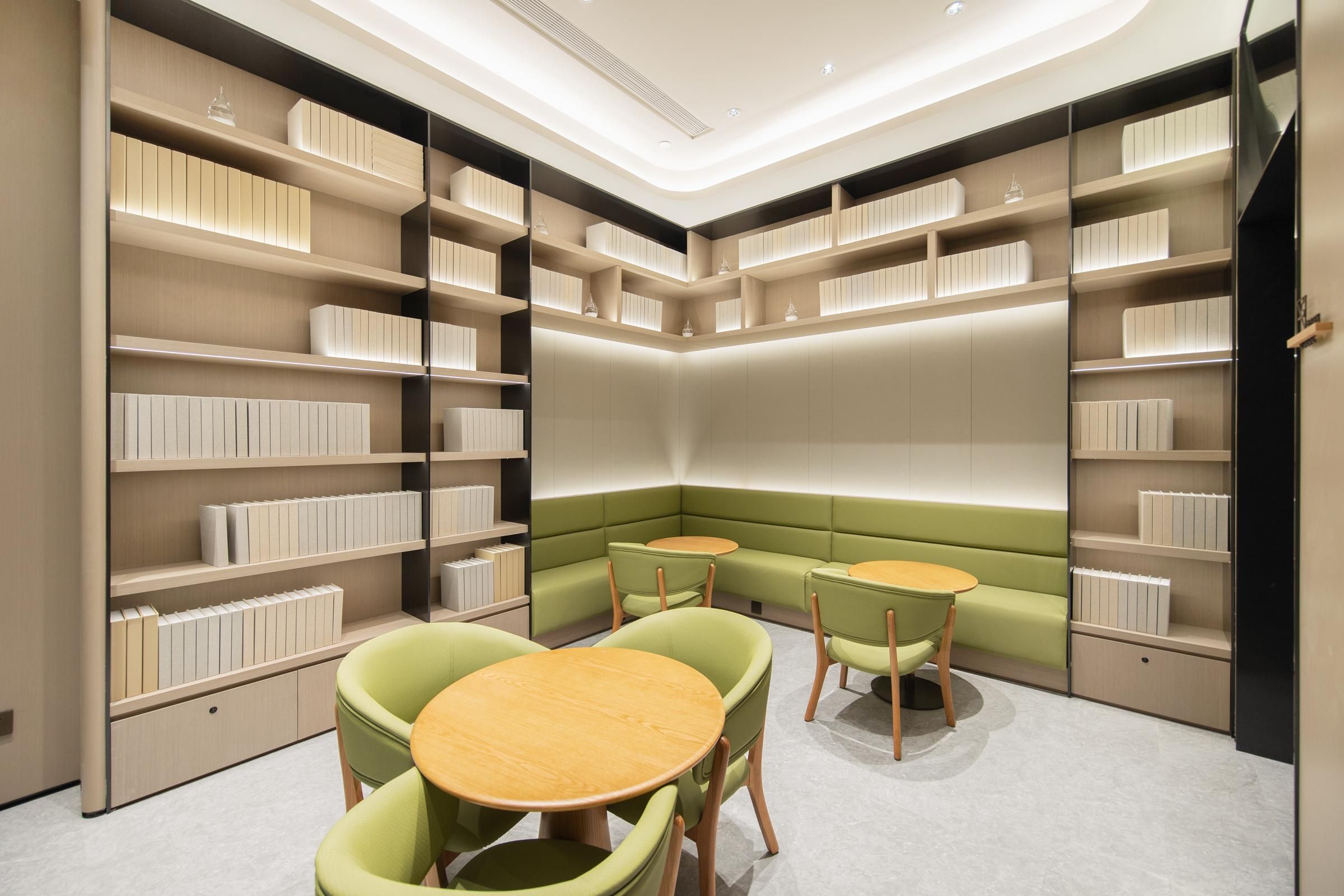 Uma biblioteca moderna com estantes, um espaço de estar verde e mesas redondas.