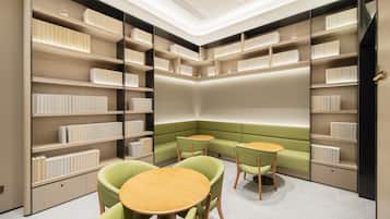 Uma biblioteca moderna com estantes, um espaço de estar verde e mesas redondas.