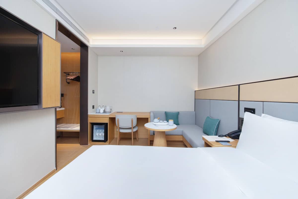 A modern hotel room with a bed, a desk with a chair, a small table, and a sofa.