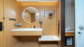 Un baño moderno con tocador de madera, un espejo redondo, un perchero para toallas y un refrigerador pequeño.