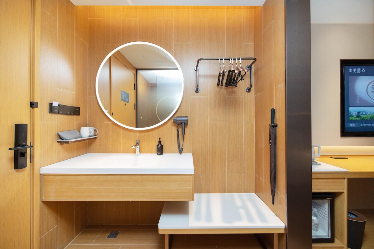 A modern bathroom with a wooden vanity, a round mirror, a towel rack, and a small shelf with a cup.