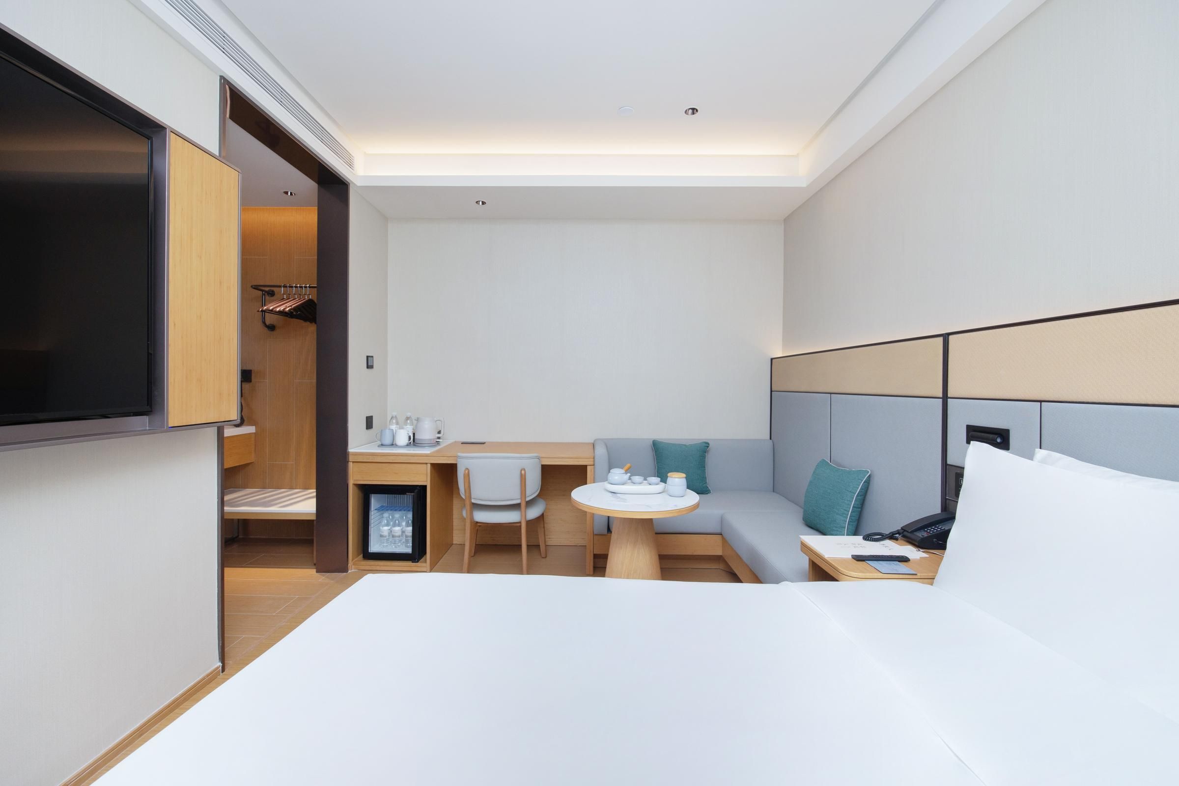 Una habitación de hotel moderna con cama, escritorio con silla, una mesita y un sofá.