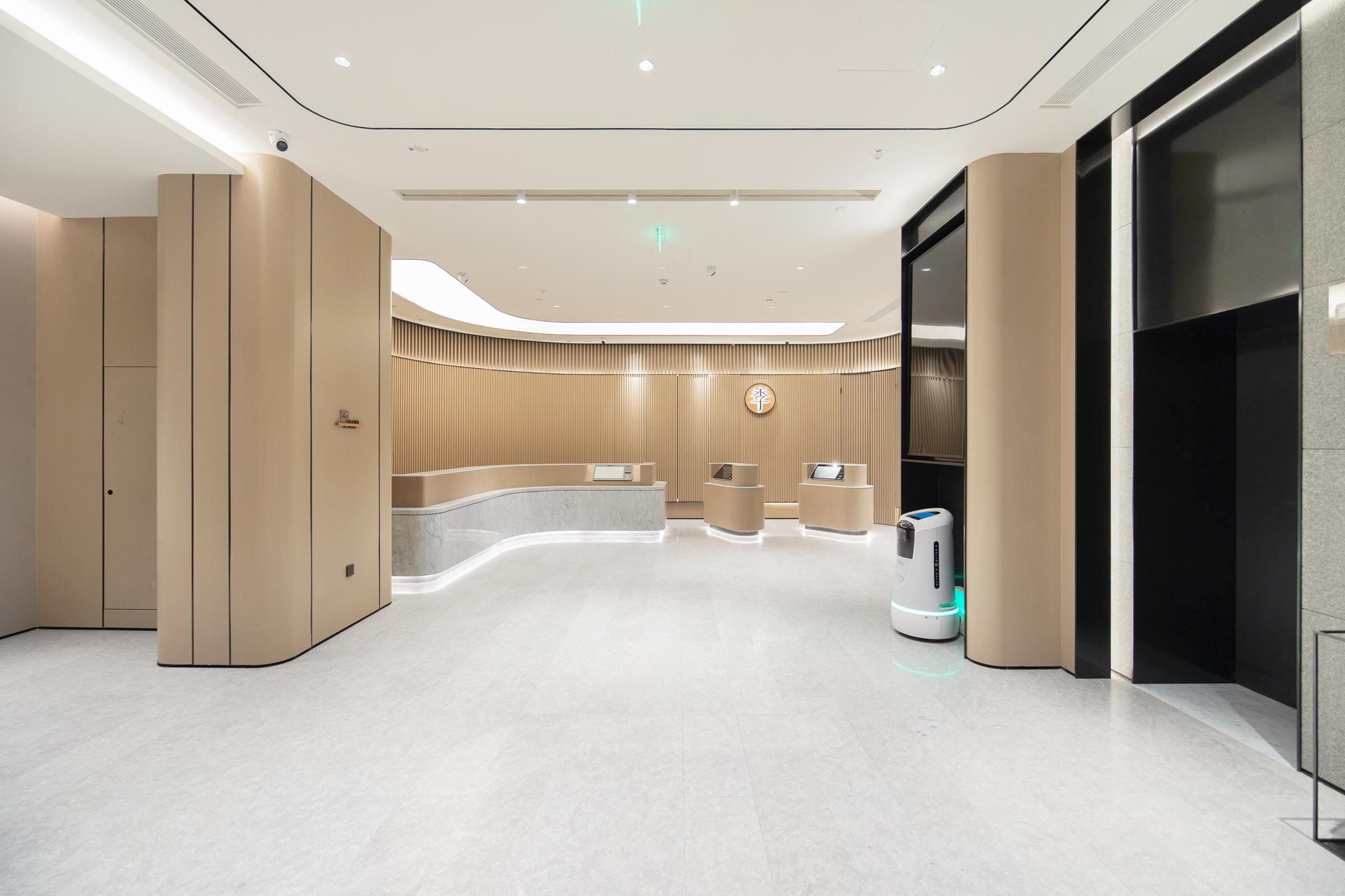 Un hall d’hôtel moderne doté d’un comptoir d’accueil incurvé, d’un kiosque en libre-service et d’un aspirateur robot.