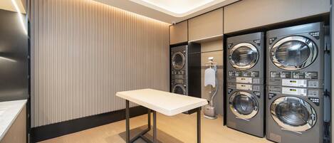 A modern laundry room with a table, two wall-mounted washing machines, and a ceiling light.