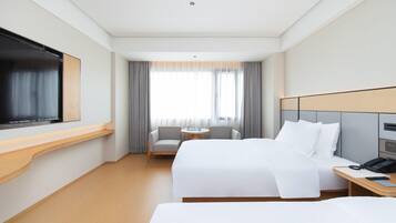Habitación de hotel con cama, televisión, escritorio con teléfono, silla y ventana con cortinas.