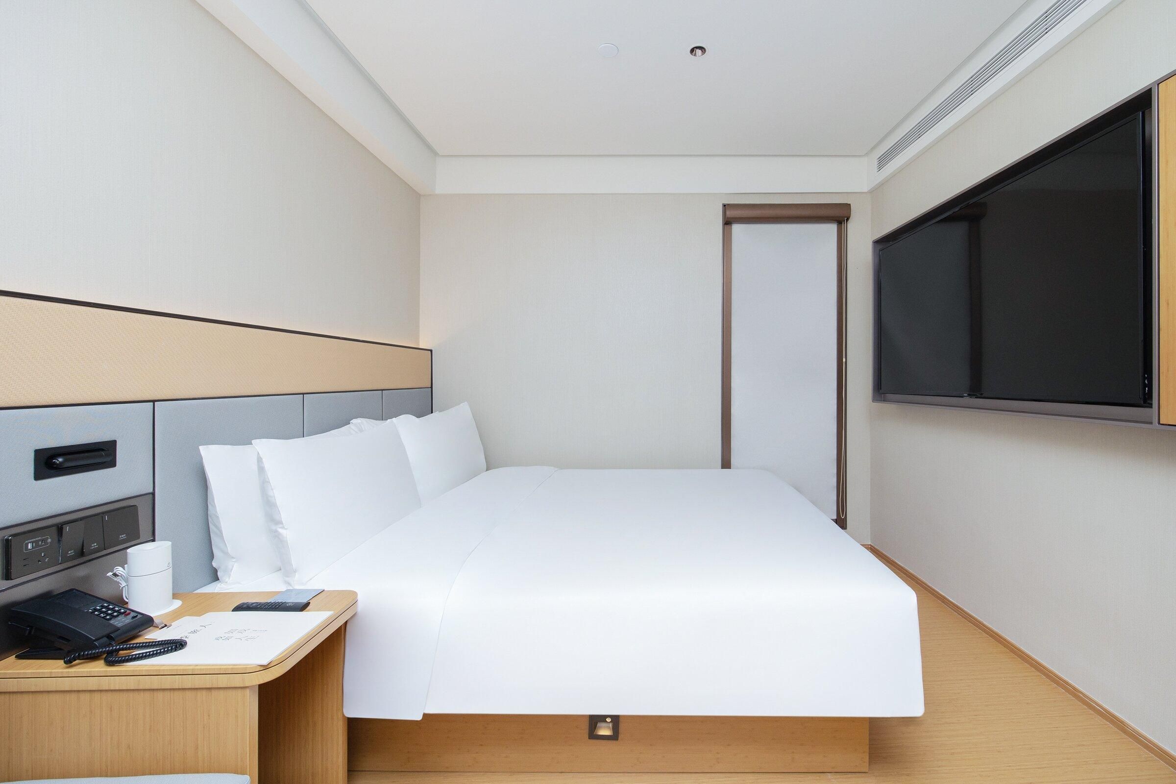A hotel room with a bed, bedside table, TV, and a door.