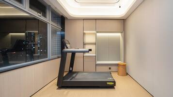 Una habitación moderna con una cinta de correr, una ventana con vistas a la ciudad, un taburete de madera pequeño y una estantería empotrada.