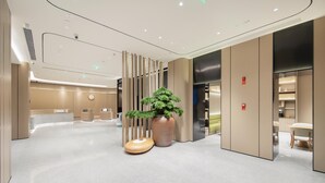 Eine moderne Hotelhalle mit einer Rezeption, einer großen Topfpflanze und einer Sitzecke.