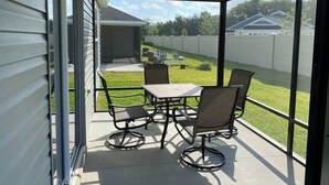 Eine überdachte Terrasse mit Tisch und Stühlen, einem Deckenventilator und Blick auf einen Garten mit Rasen und Zaun.