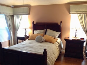 A neatly made bed with a wooden headboard, two bedside tables with lamps, and curtains on the windows.