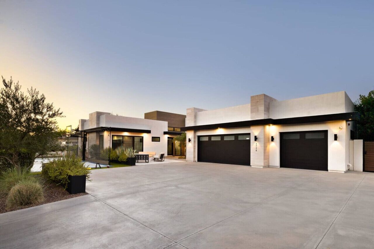 Een modern huis met twee verdiepingen, een ruime oprit, garage deuren en een buiten zitplaats.