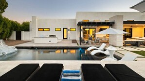 Un espace piscine extérieur moderne, doté de chaises longues, d’un barbecue et d’un coin salon abrité.
