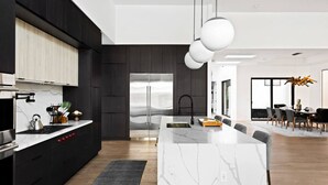 Une cuisine moderne dotée d’un grand îlot central, de meubles de couleur sombre et d’appareils électroménagers en acier inoxydable.