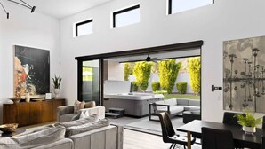 Un salon moderne avec un canapé gris, une table à manger et des chaises, et une grande fenêtre donnant sur un jardin.