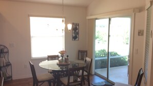 A dining area with a round table, chairs, and a vase of flowers. There is a window with blinds and a door leading to a balcony. - 2067 Useppa Oaks Ln (Wildwood)