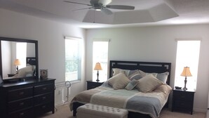 A bedroom with a bed, a dresser, a mirror, two bedside lamps, and a ceiling fan. - 2067 Useppa Oaks Ln (Wildwood)