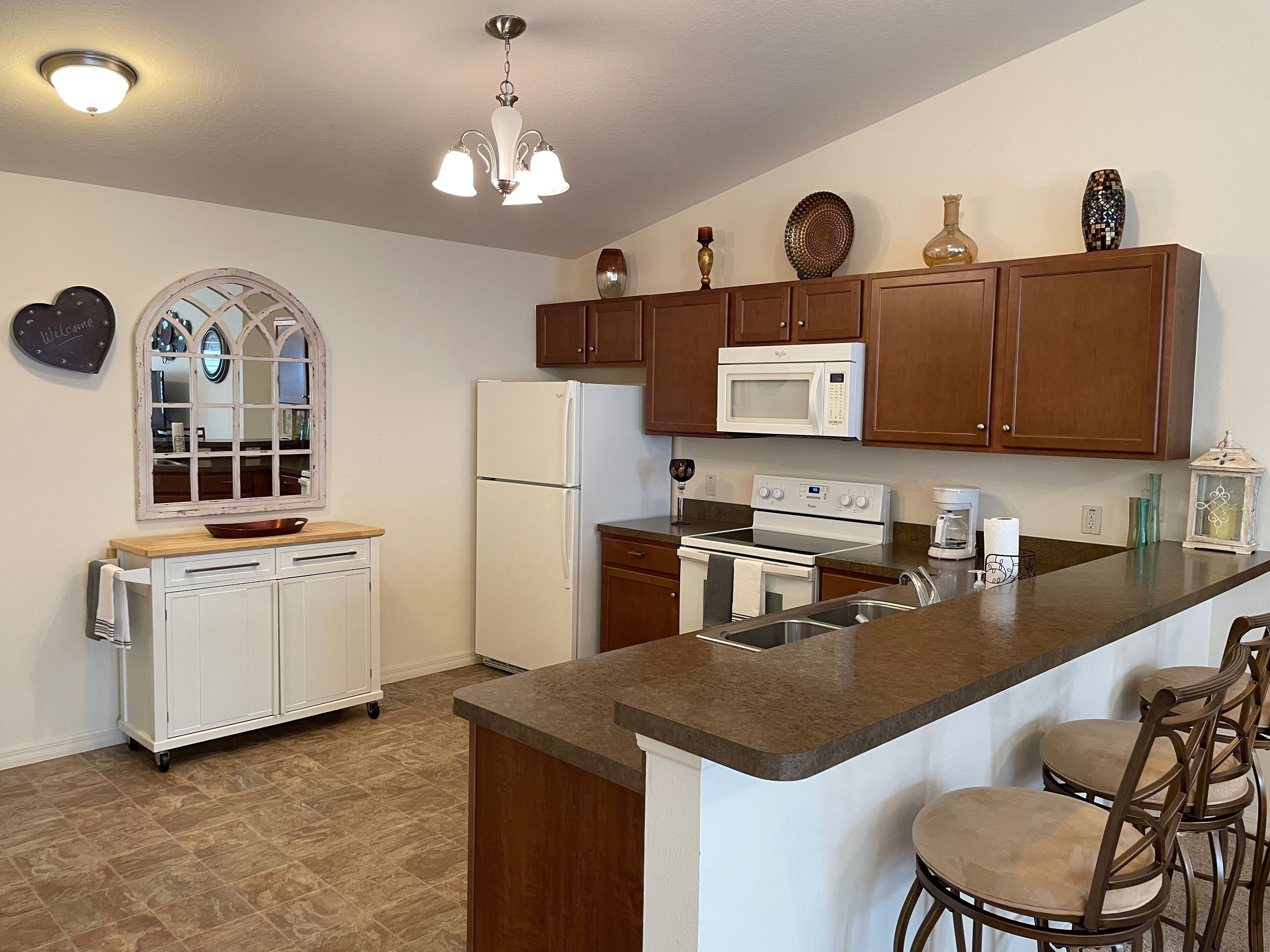 A kitchen with a central island, wooden cabinets, a microwave, stove, and a refrigerator.