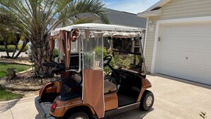 En golfvogn parkeret i en indkørsel med et hus i baggrunden.