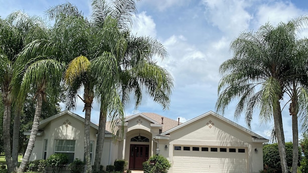 A two-story house with a garage, surrounded by palm trees and a well-maintained lawn. - 1468 Tidewater Ter (The Villages)