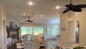 A spacious living room with a fireplace, a dining area with a table and chairs, and a kitchen area with a refrigerator. - 1468 Tidewater Ter (The Villages)