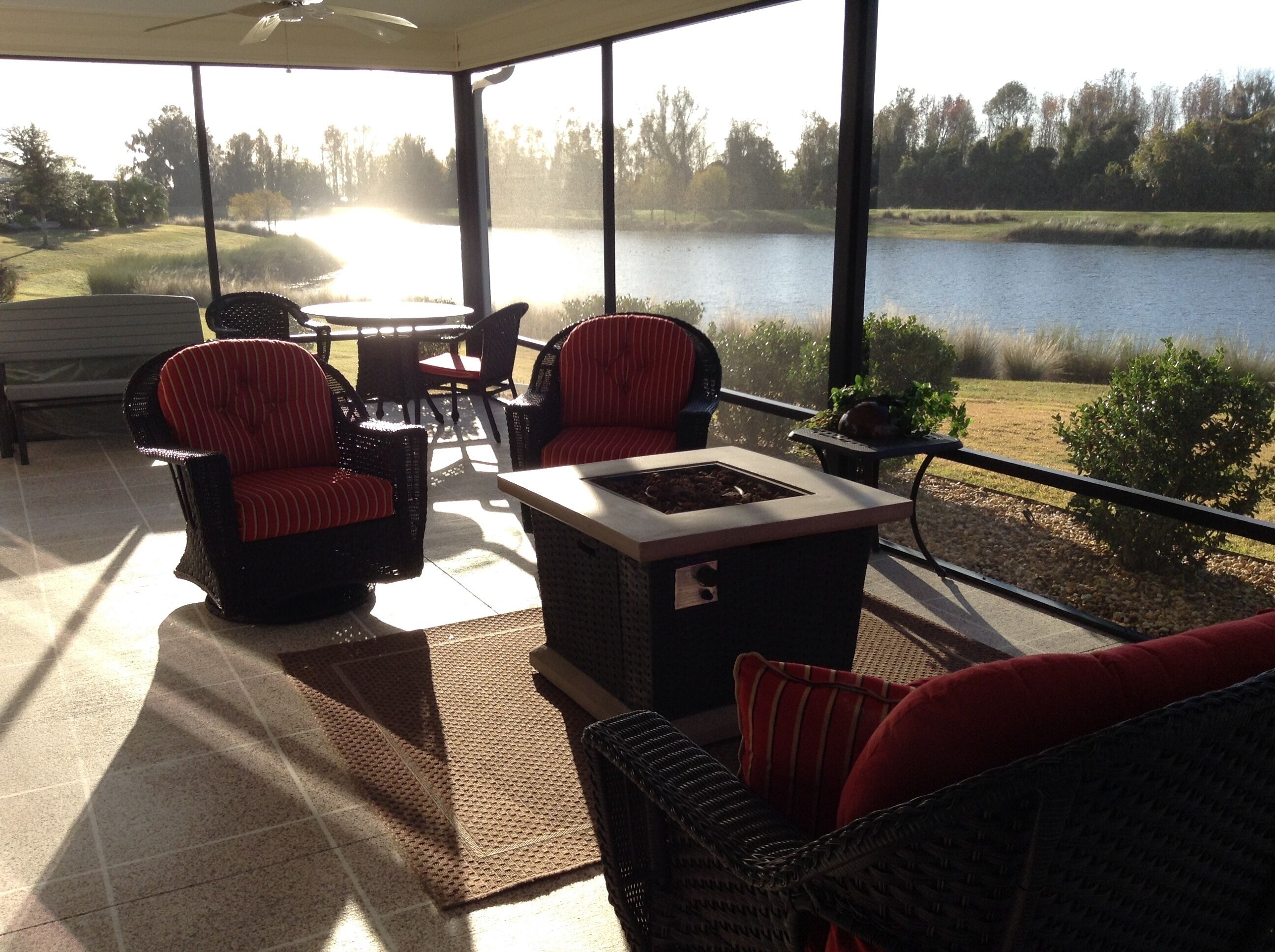 A covered patio with wicker furniture, a fire pit, and a view of a lake.