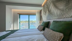 Hotelkamer met een groot bed, uitzicht op een jachthaven en een hoofdeinde in tropisch thema.